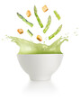 Asparagus and croutons falling into a creamy soup bowl splashing on white background.