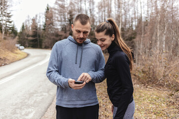 Two young people checking their fitness progress on a smartphone app after a morning run.