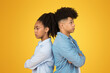 A teenage girl and boy stand back-to-back with arms crossed and displeased expressions, against a yellow background