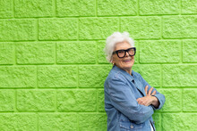 Elderly Lady In Denim Jacket Standing Against A Lime Green Wall