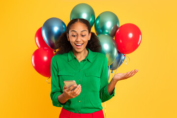 Wall Mural - Excited African teenager girl texting on phone with balloons, studio