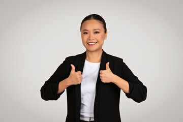 Smiling Asian businesswoman in a black blazer giving two thumbs up as a sign of approval