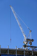 Hoisting tower crane on the top section being constructed of modern high skyscraper building against blue cloudless sky