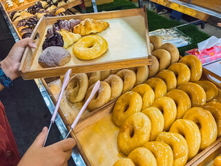 Woman buying donuts in baking store. Female choosing and buying fresh tasty pastry from shelves. Young woman choose freshly baked donuts in street food bakery. Customer buy doughnut. Selective focus.