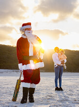 Santa Claus On The Beach With A Cricket Bat With Young Woman And Baby Looking On