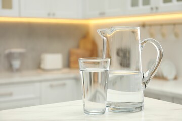 Poster - Jug and glass with clear water on white table in kitchen, space for text