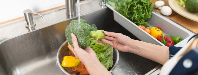 Wall Mural - Close up of hands people washing vegetables by tap water at the sink in the kitchen to clean ingredient prepare a fresh salad.