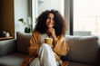 © wolfhound911 - Latin woman drinking coffee sitting on sofa at home