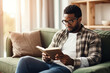 © wolfhound911 - Pensive relaxed African American man reading a book at home, drinking coffee sitting on the couch. Copy space