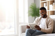 © wolfhound911 - Pensive relaxed African American man reading a book at home, drinking coffee sitting on the couch. Copy space