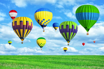 Wall Mural - Bright hot air balloons flying in sky with clouds over green meadow