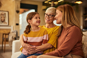 Wall Mural - A smiling little girl sitting on her grandma's lap, spending time with grandma and mother.