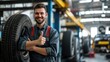 Smiling mechanic showing thumbs up with car tire in the car repair shop.
