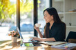 © Wasana - Freelance Asian woman enjoying morning coffee during break from work with sunlight shining through the glass on her table.