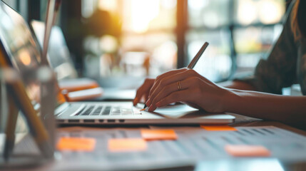 Wall Mural - Hands of a person typing on a laptop keyboard with a blurred background of stacked files and documents