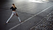 © WellStock - Back view of strong sportswoman in stylish training clothes warming up and doing stretch exercises at the street in summer day morning. Healthy and sport concept