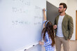 © zinkevych - School teacher watching pupil writing on white board in classroom.