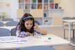 © zinkevych - Dark haired little girl pupil sitting in classroom doing tasks.