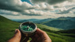 © anandart - Compass in man's hand in front of summer mountain landscape with green hills and cloudscape , travel adventure and discovery consept