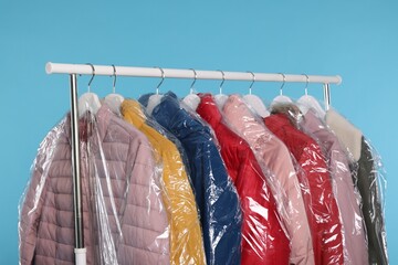 Wall Mural - Dry-cleaning service. Many different clothes in plastic bags hanging on rack against light blue background