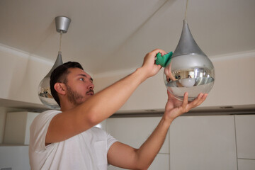 Wall Mural - Extreme close-up of unrecognizable man cleaning electric lamp with wet microfiber rag. Close-up of male hands wiping chandelier removing dust at home. Concept of cleaning and household, slow motion.