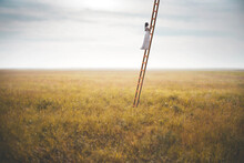 Woman Climbing A Surreal Ladder In The Middle Of A Field Reaching The Sky, Abstract Concept