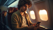 © scaliger - Young man uses mobile phone sitting in flying airplane, guy passenger browsing social media on smartphone inside plane. Concept of travel, flight, internet, technology, trip,