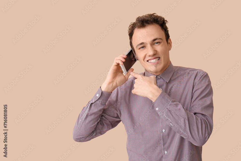 Young man talking by smartphone on beige background
