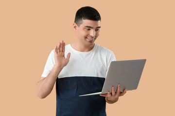 Poster - Young man with laptop video chatting on beige background