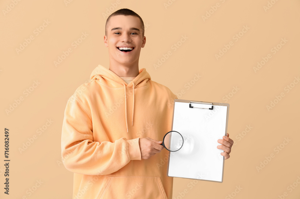 Young man with magnifier and clipboard on beige background