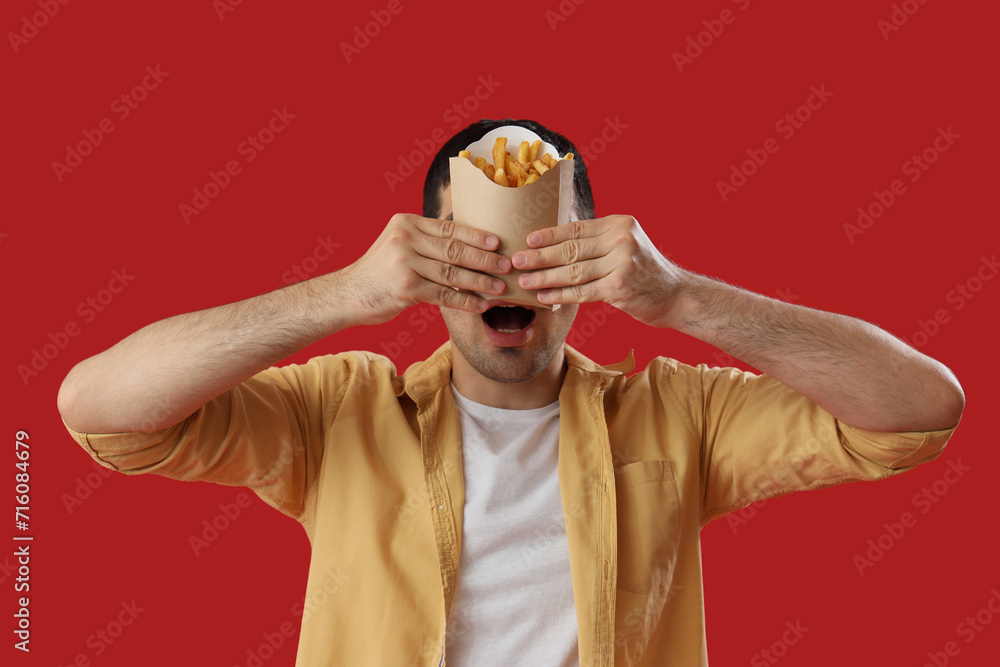 Shocked young man with french fries on red background