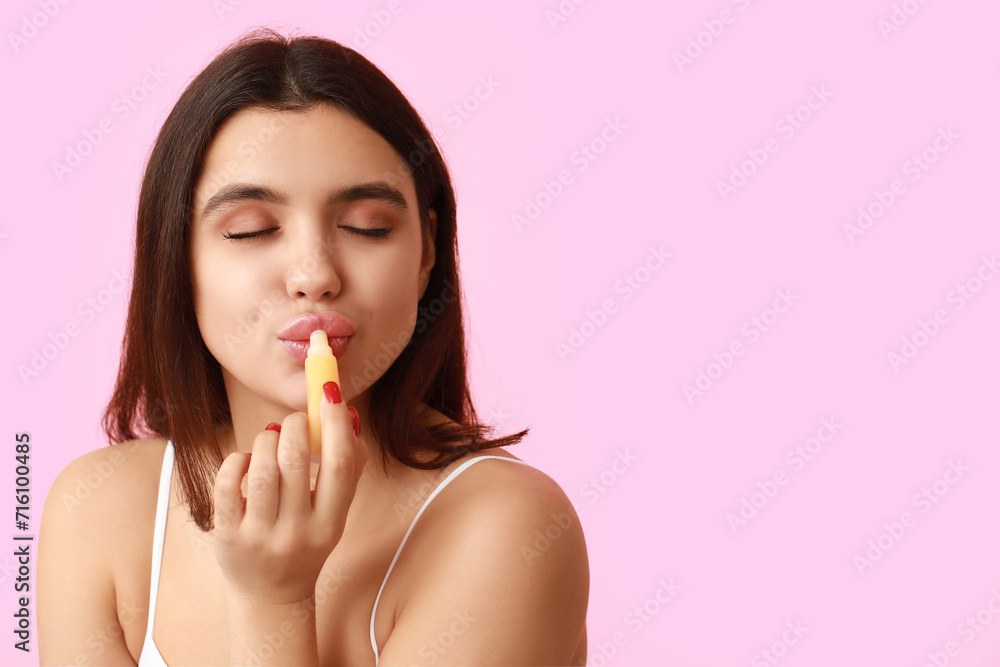 Beautiful young woman applying lip balm on pink background