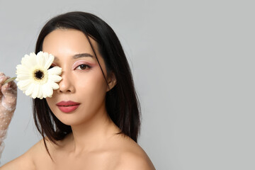 Poster - Beautiful young Asian woman with white gerbera flower on grey background