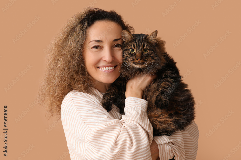 Happy mature woman with cute cat on brown background