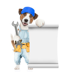 Poster - Funny jack russell terrier puppy wearing blue cap and denim overalls with tool belt shows empty list and wrench. Isolated on white background