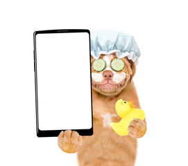 Poster - Mastiff puppy wearing shower cap with pieces of cucumber on it eyes and with cream on it face holds  rubber suck and big smartphone with white blank screen in it paw. isolated on white background