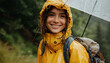 A positive girl smiling wearing a raincoat jacket with a hood, enjoying the rain with an umbrella outdoors.