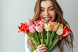 Happy young woman with bouquet of beautiful tulips on light background