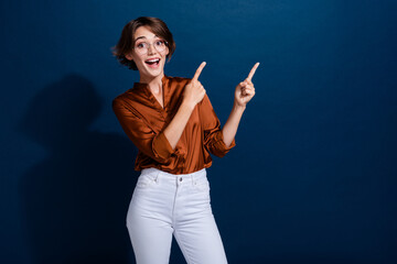 Sticker - Photo of cheerful surprised girl dressed stylish clothes presenting brand product empty space isolated on dark blue color background