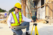 © ฺฺฺBoonterm - Female engineer foreman sitting holds laptop computer setup and checks  modern technology tools laser level and vertical marker (Plum Bob) on tripod at construction site, condominium building.