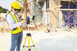 © ฺฺฺBoonterm - Female engineer foreman holds laptop computer setup and checks  modern technology tools laser level and vertical marker (Plum Bob) on tripod at construction site, condominium building.