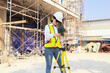 © ฺฺฺBoonterm - Female engineer foreman holds laptop computer setup and checks  modern technology tools laser level and vertical marker (Plum Bob) on tripod at construction site, condominium building.