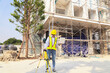 © ฺฺฺBoonterm - Female engineer foreman holds laptop computer setup and checks  modern technology tools laser level and vertical marker (Plum Bob) on tripod at construction site, condominium building.