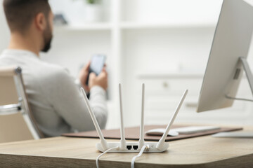 Man with smartphone working at wooden table indoors, focus on Wi-Fi router