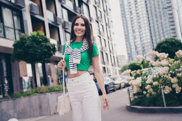 Poster - Photo of young charming positive happy attractive woman wear white knitted handbag green crop top with pants walking in city outside