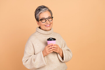 Sticker - Portrait of positive aged person toothy smile hold fresh coffee cup empty space isolated on beige color background