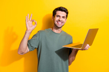 Sticker - Photo of satisfied man with bristle dressed khaki t-shirt holding laptop showing okey good job isolated on vibrant yellow color background