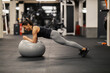 © dusanpetkovic1 - Side view of a sportswoman doing planks on fitness ball in a gym.