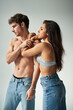 © LIGHTFIELD STUDIOS - beautiful young woman in satin bra and jeans embracing shirtless man on grey background, affection