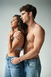 © LIGHTFIELD STUDIOS - shirtless man and brunette woman in denim jeans embracing while standing on grey background